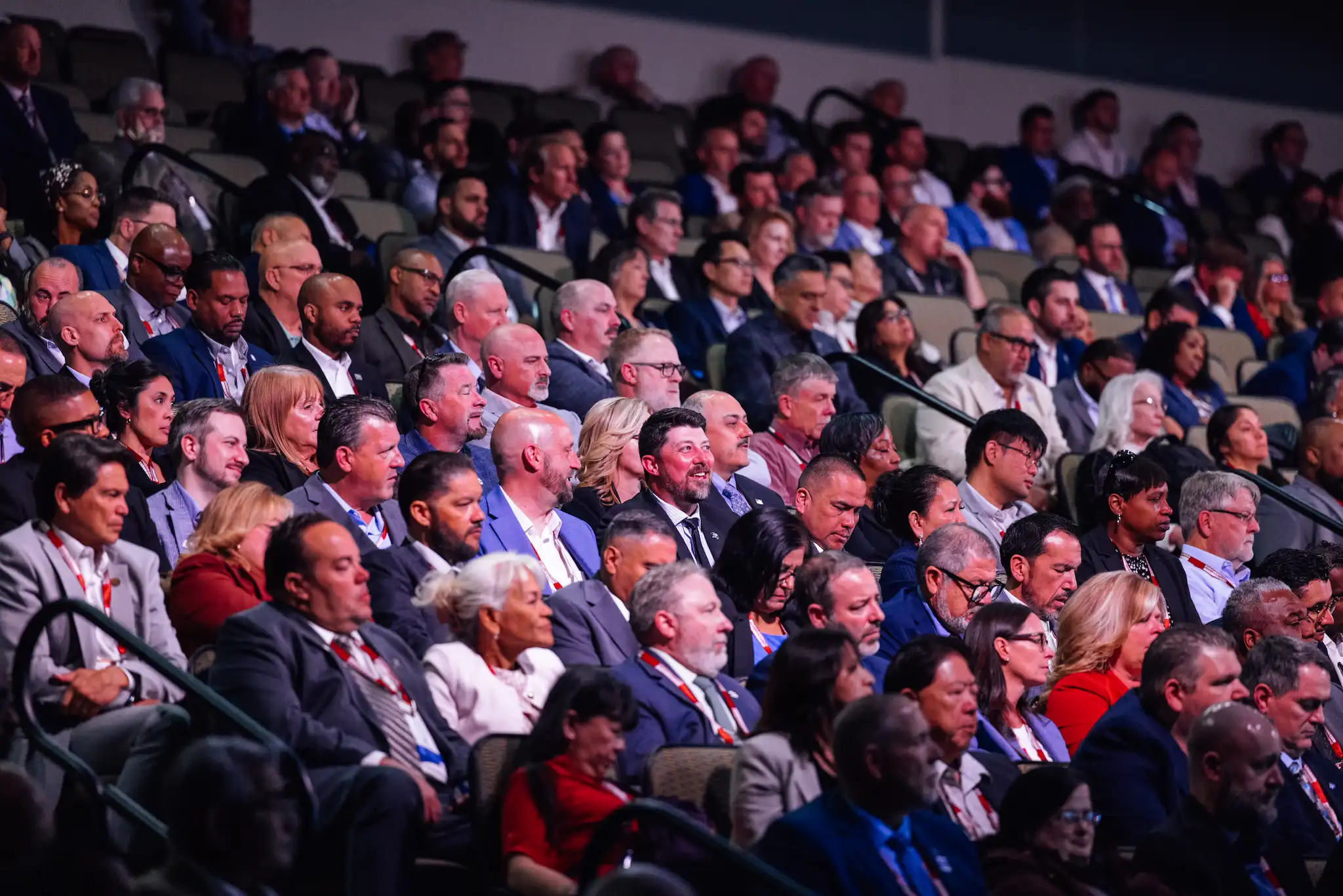 Large crowd seated facing a stage with a blue screen showing United States Postal Service logo.
