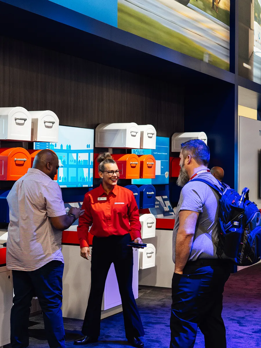 Three people talking inside a store with colorful mailboxes displayed on the wall behind them.