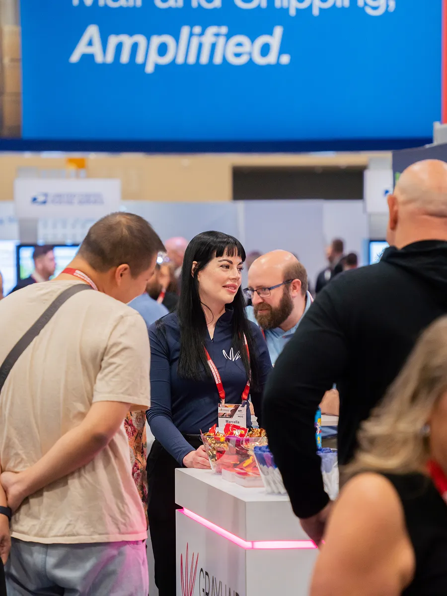 People interacting at a booth with a woman wearing a name tag that says Marcella at a trade show.