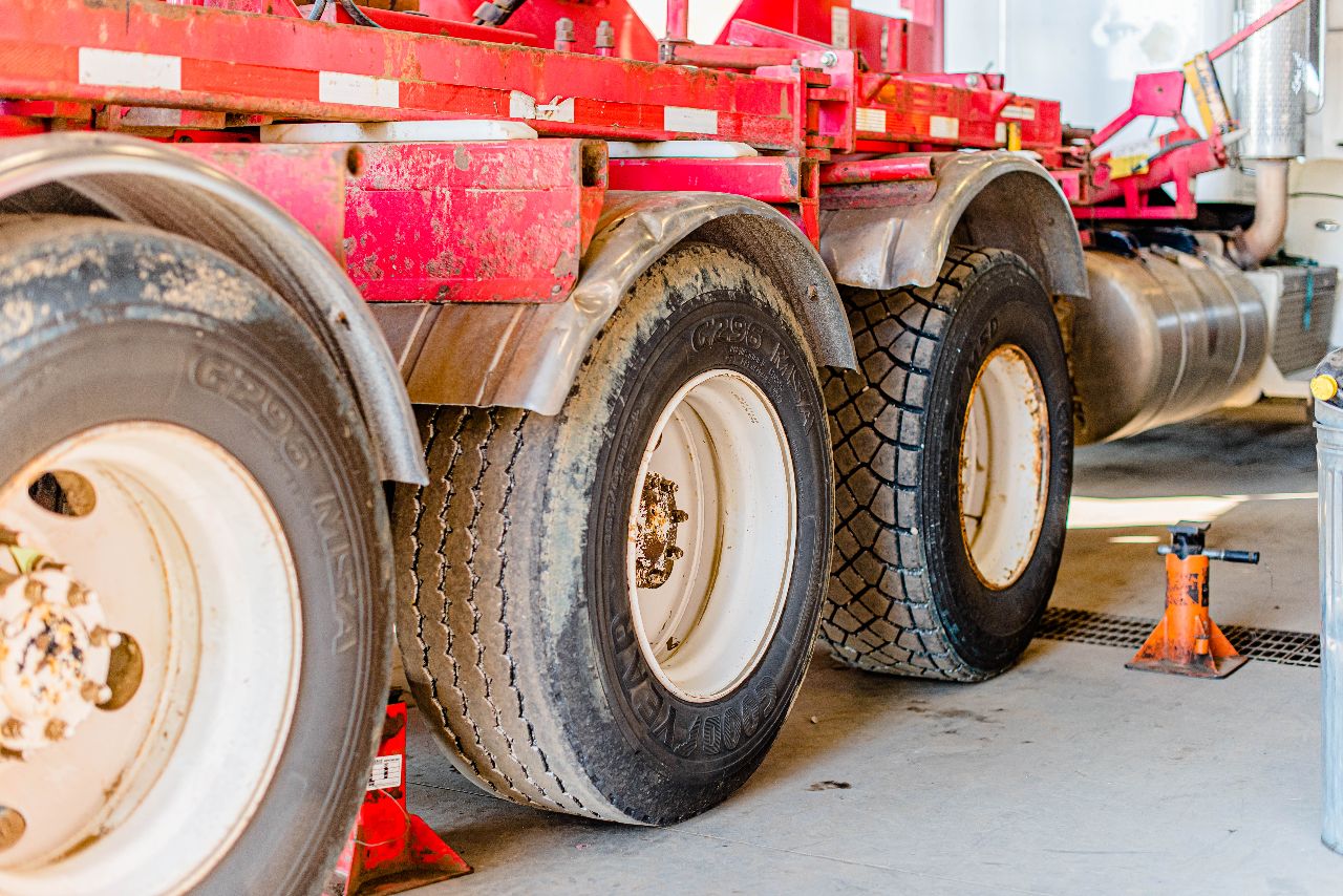 Close-up of a heavy-duty truck’s rear tires lifted on jack stands in a repair shop, showing worn and clean treads. 