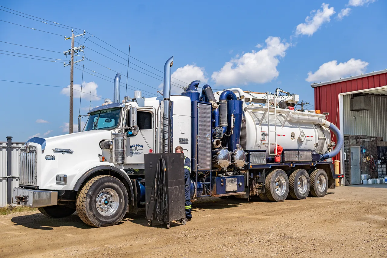 Oilfield truck parked outside a repair shop, equipped with a vacuum tank and service equipment for heavy-duty operations.
