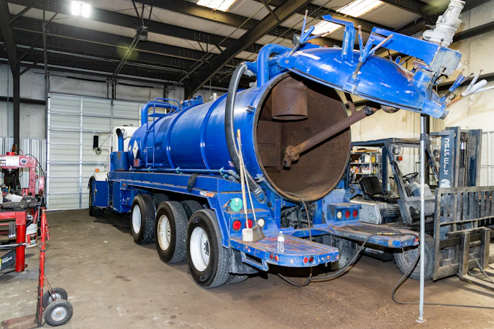Oilfield truck parked outside a repair shop, equipped with a vacuum tank and service equipment for heavy-duty operations.
