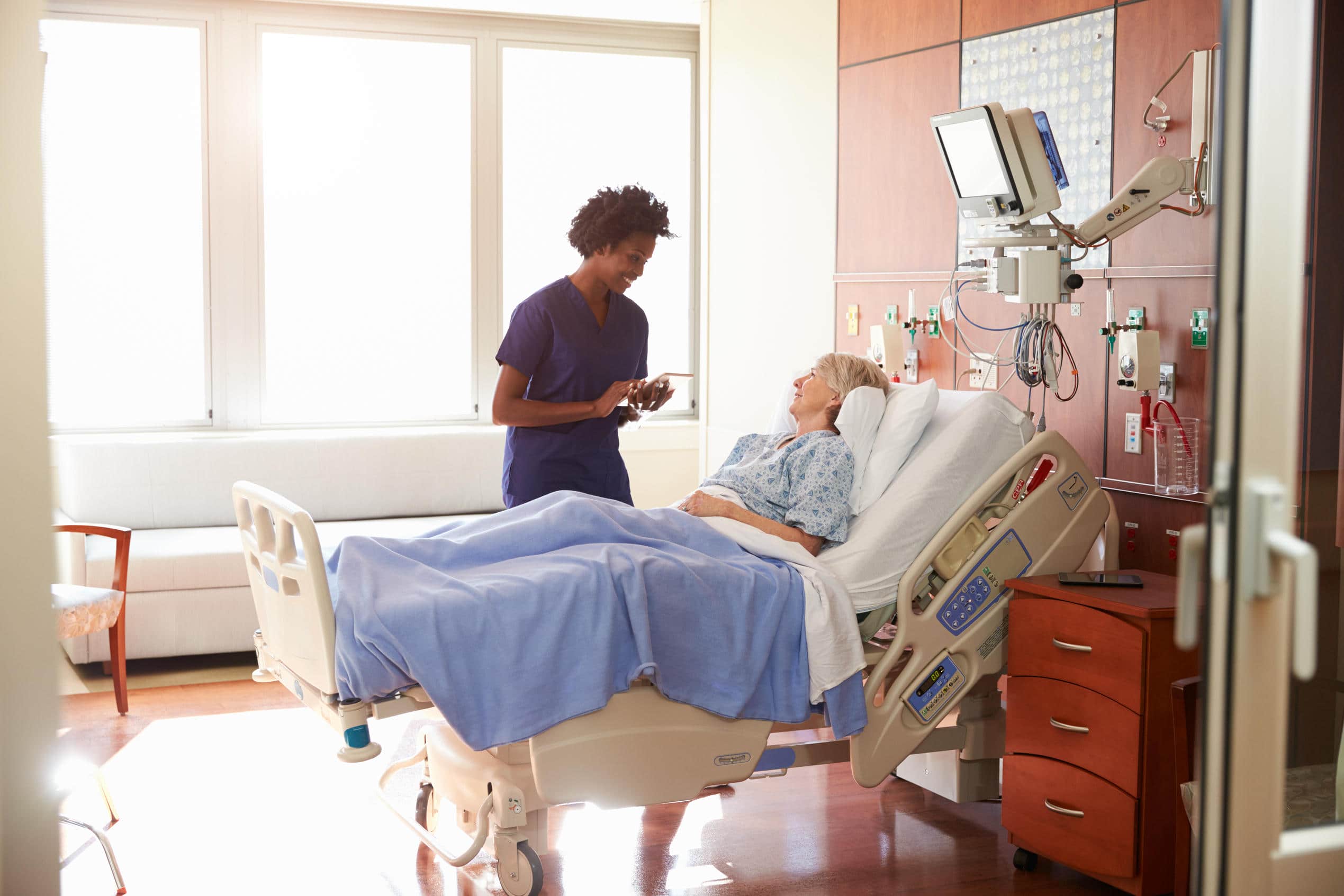 Nurse checking on an older woman resting in a hospital bed.