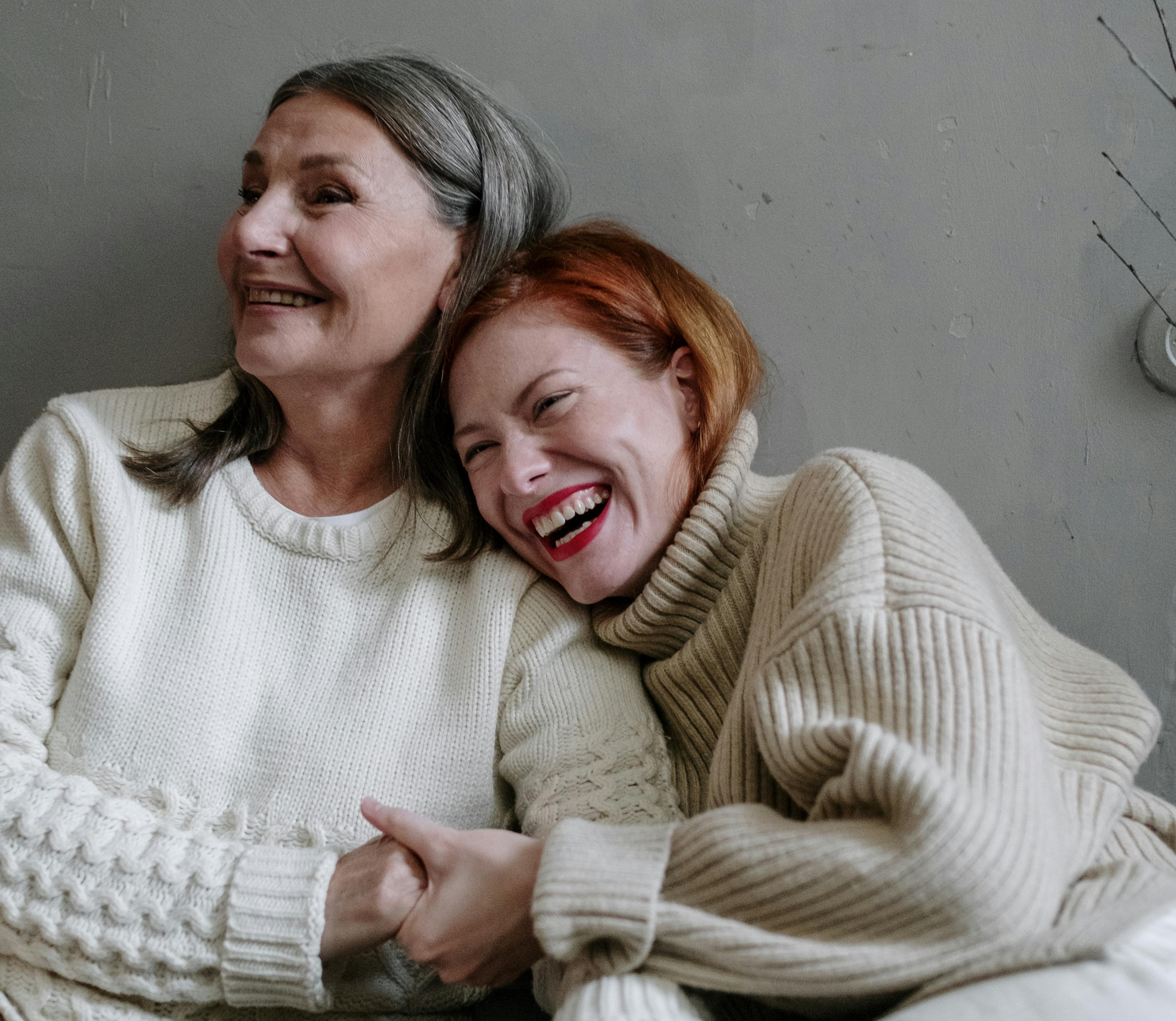 Older woman and younger woman laughing together on a couch.