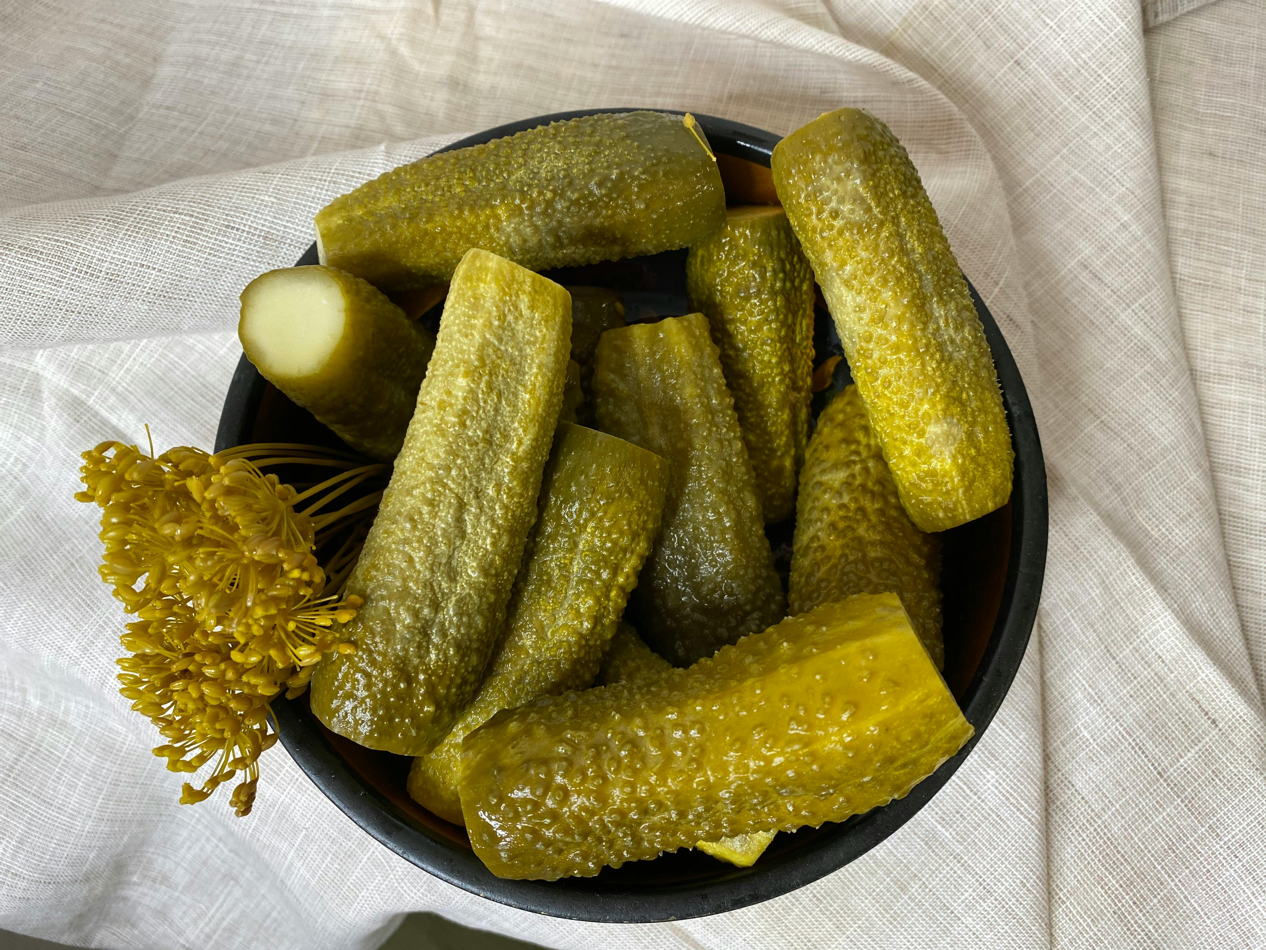 Bowl of dill pickle spears with fresh dill on a linen cloth.