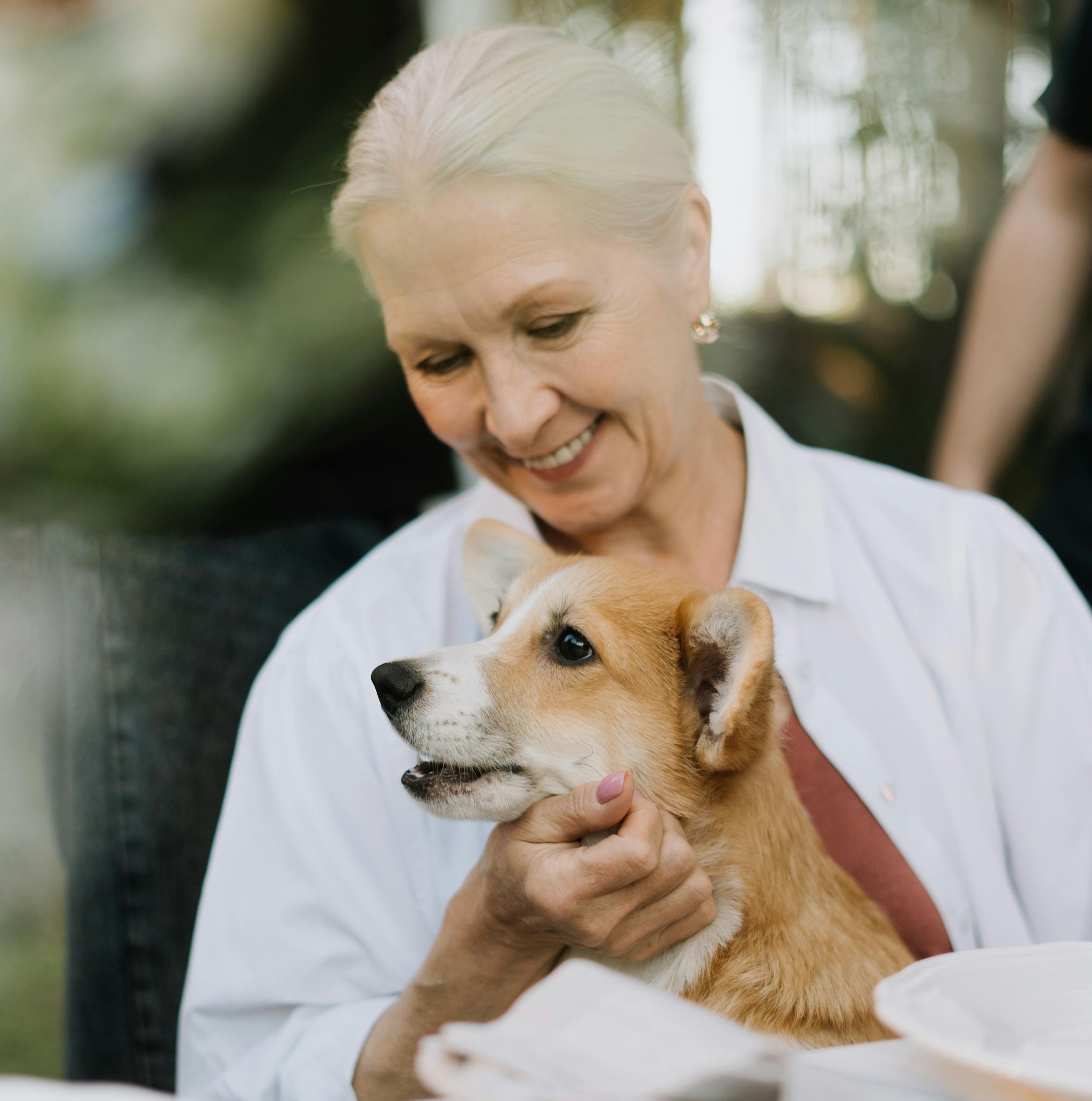 Smiling older woman hugging a corgi.