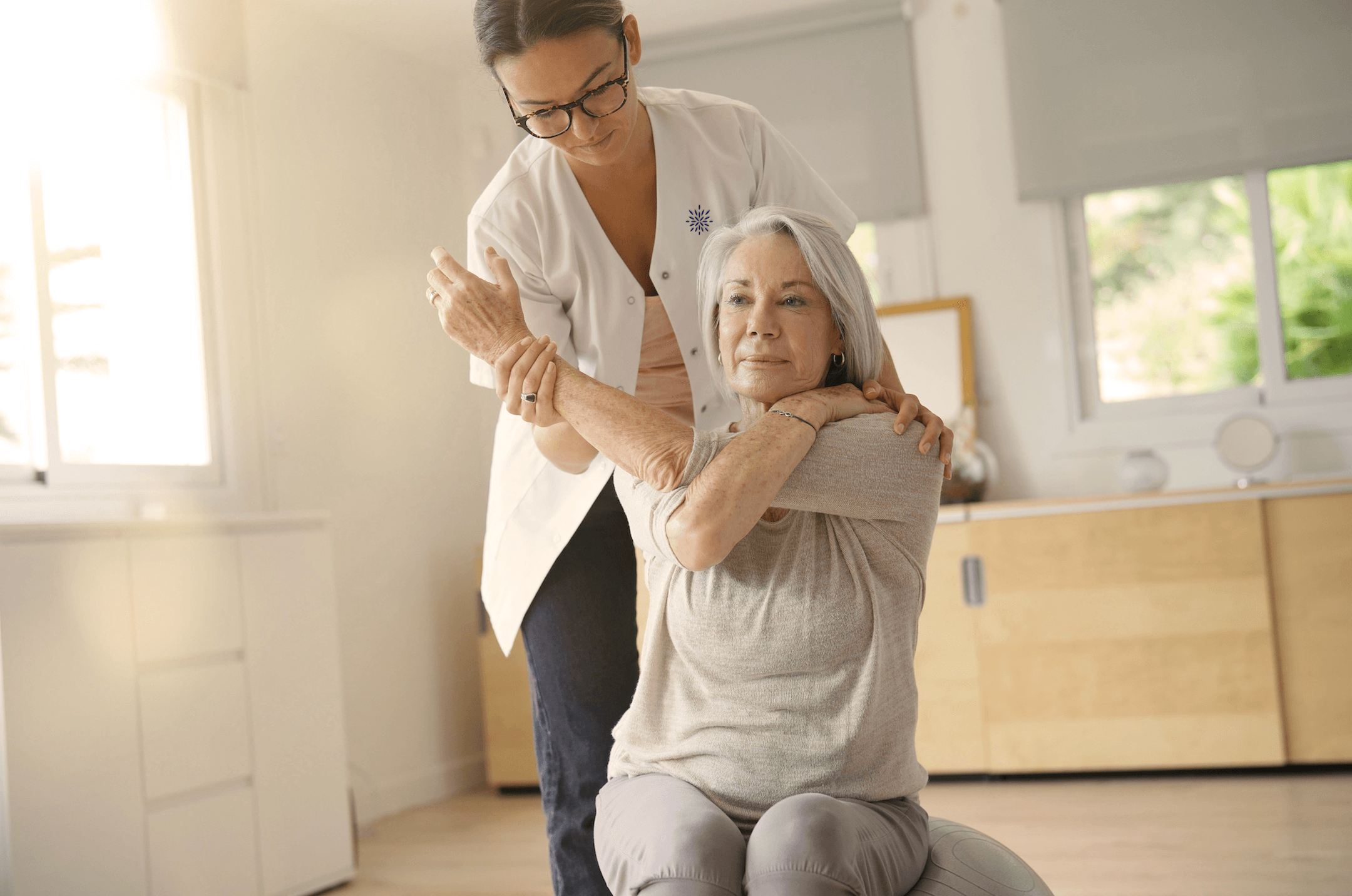 Physical therapist guiding an older woman through a shoulder stretch.