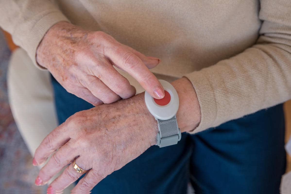 Older woman pressing the button on a wearable medical alert device.