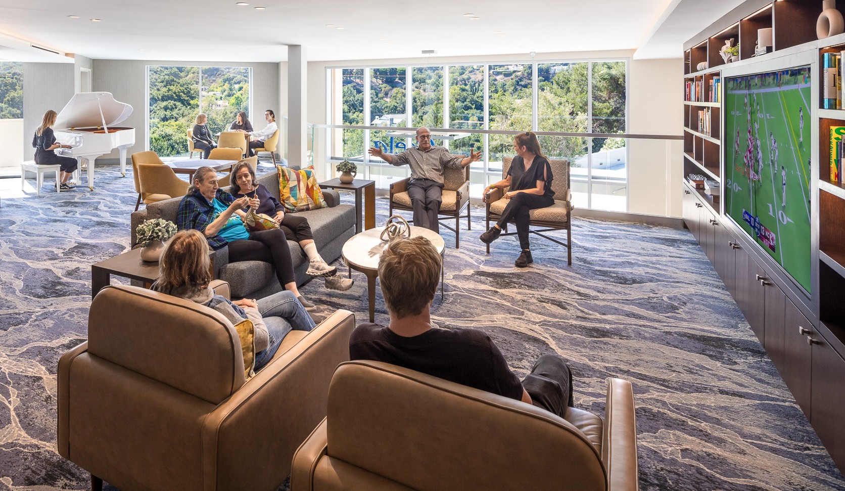Residents relaxing together in a sunlit lounge with a grand piano and bookshelves.