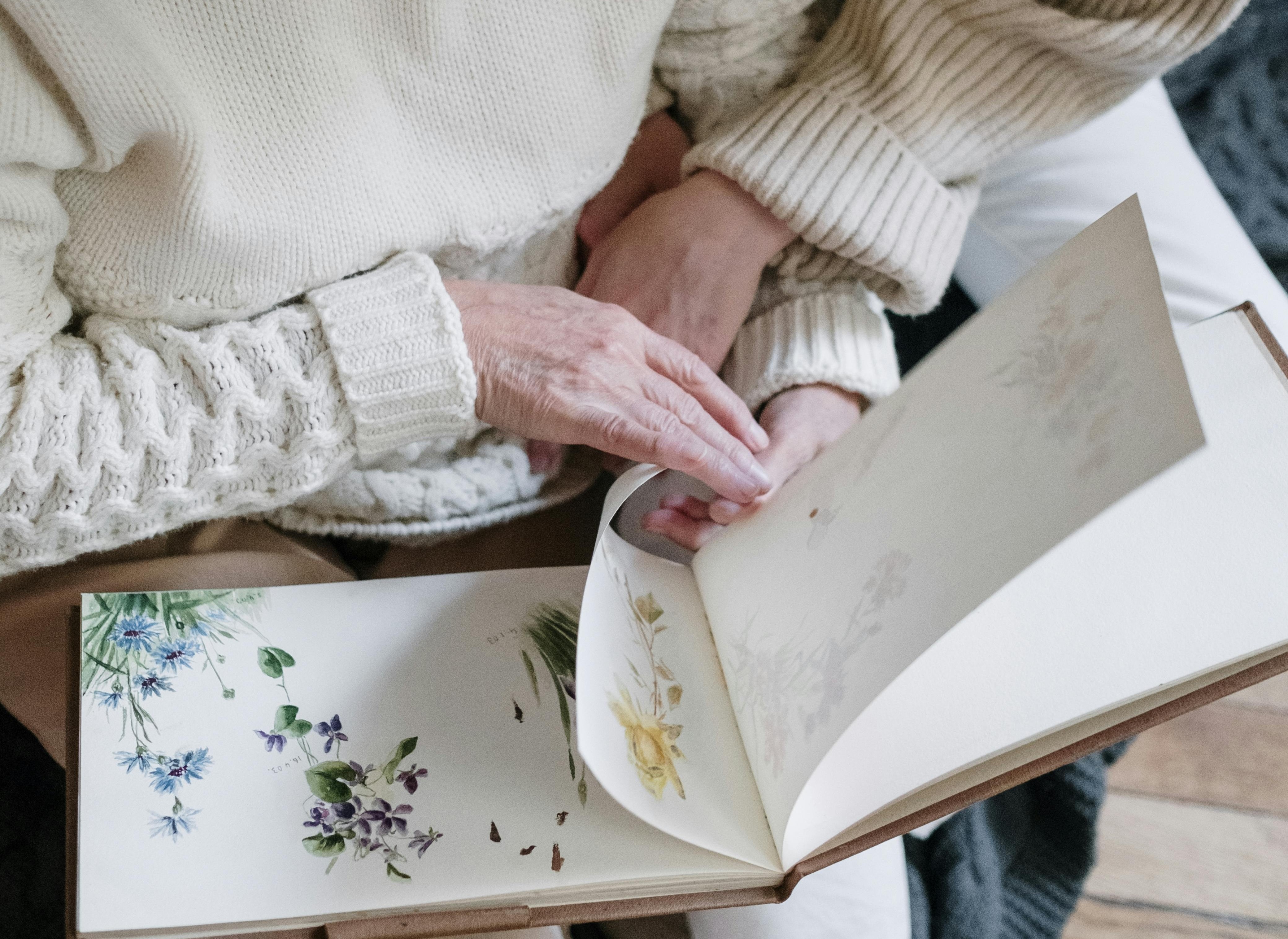 Older woman's hands paging through a sketchbook of botanical drawings.