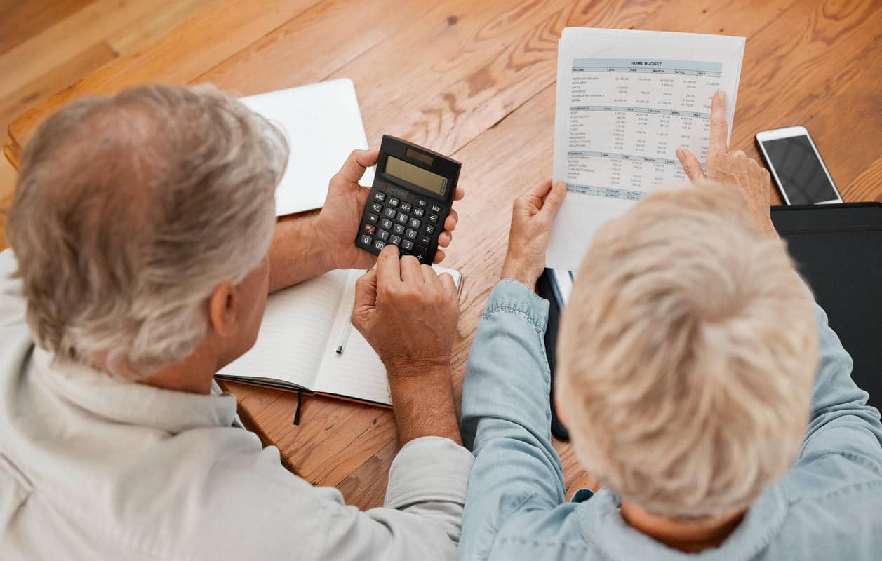 Older couple reviewing bills with a calculator at a table.