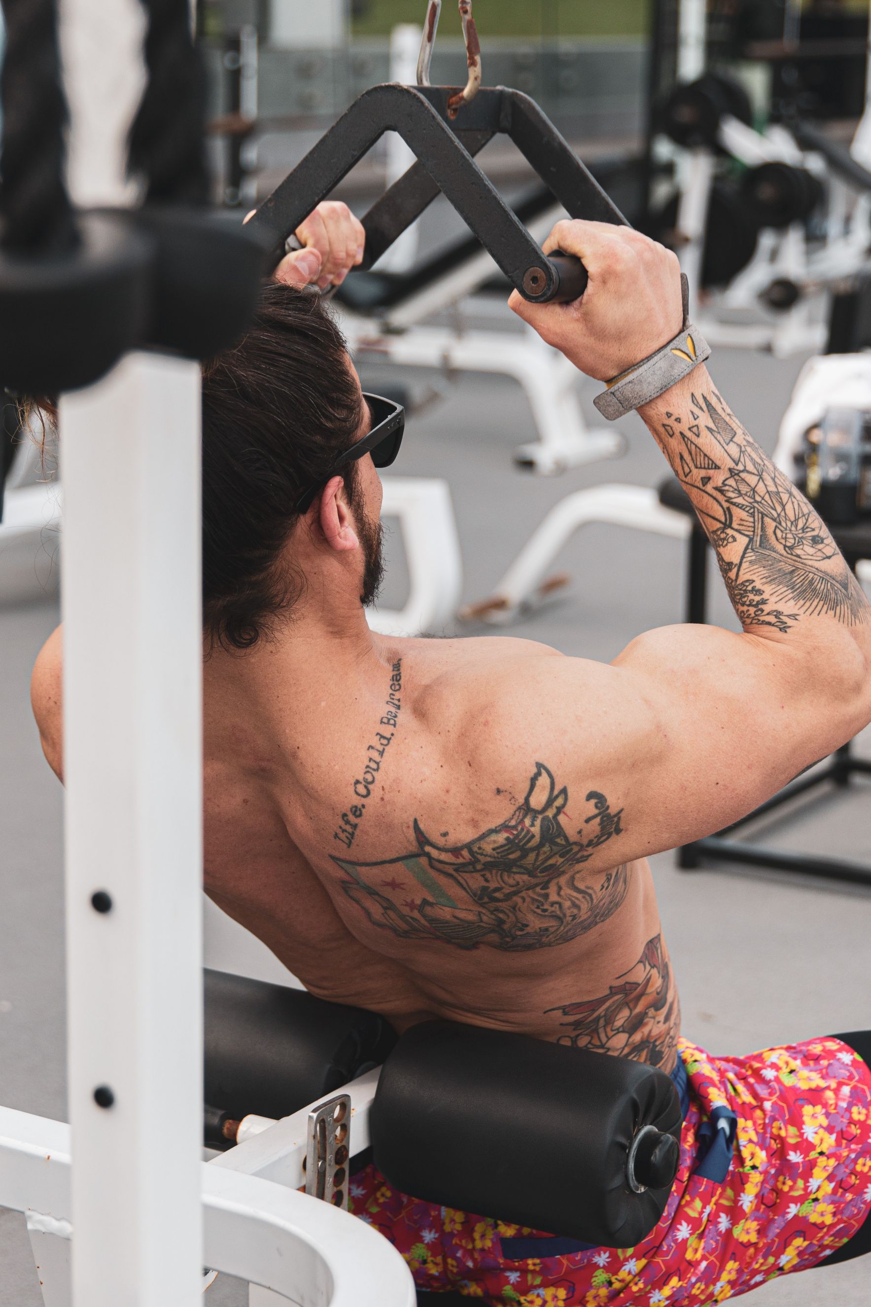 A muscular and and tattooed man using a pull-up machine in a gym.