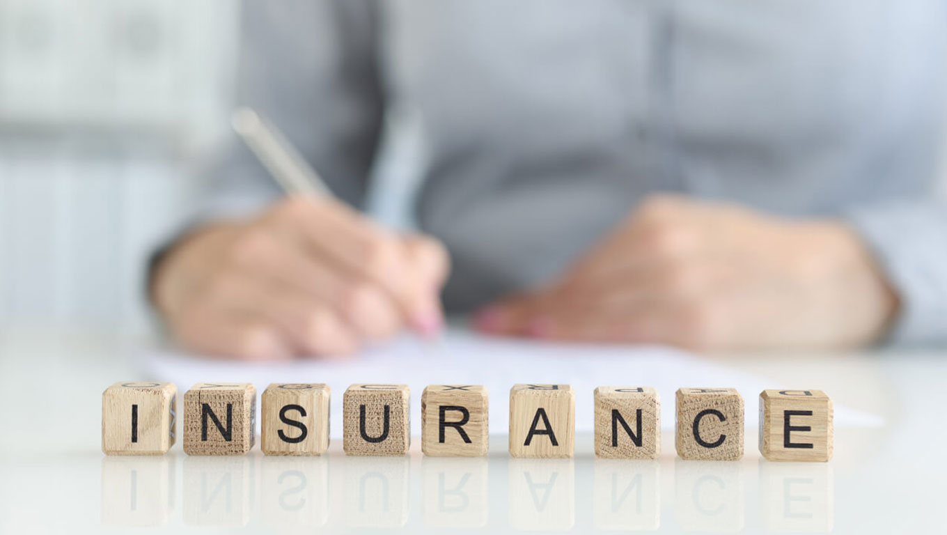 Insurance agent fills out insurance form in office closeup - insurance spelled out on wooden letter blocks