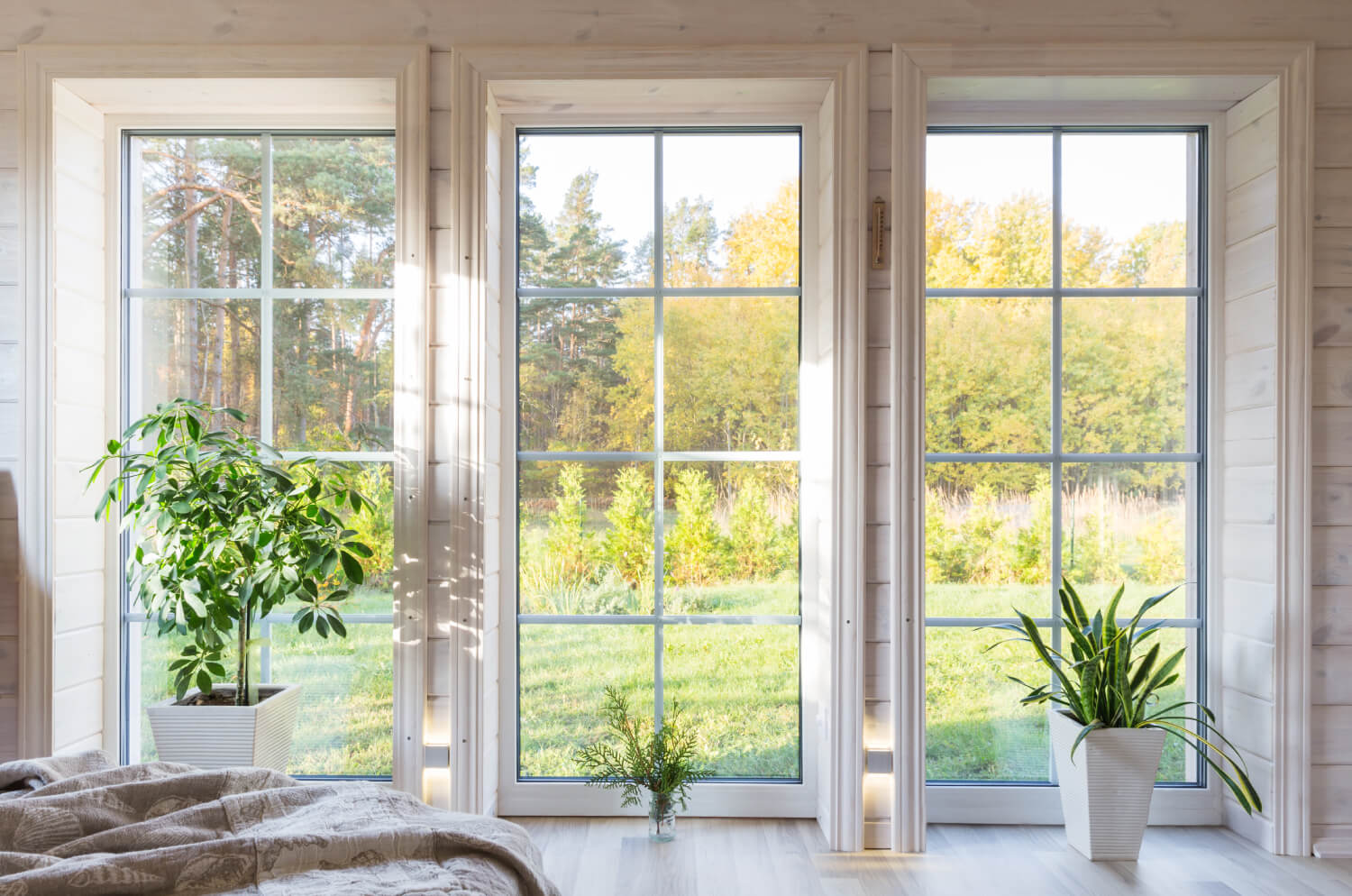 Drei bodentiefe Fenster in einem hellen Holzhaus