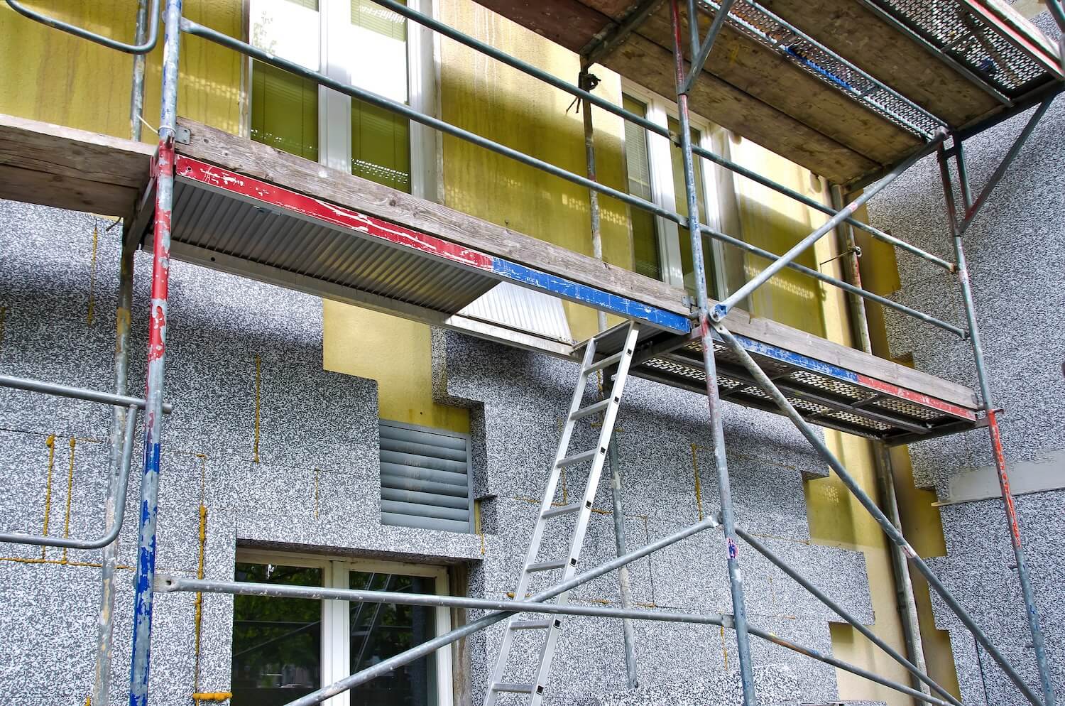 Ein Gerüst an einer Gebäudewand, auf dem Bauarbeiten stattfinden.