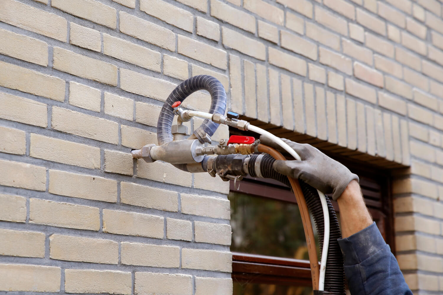 Handwerker bringt Dämmmaterial über die Einblasdämmung in das Mauerwerk eines Hauses ein