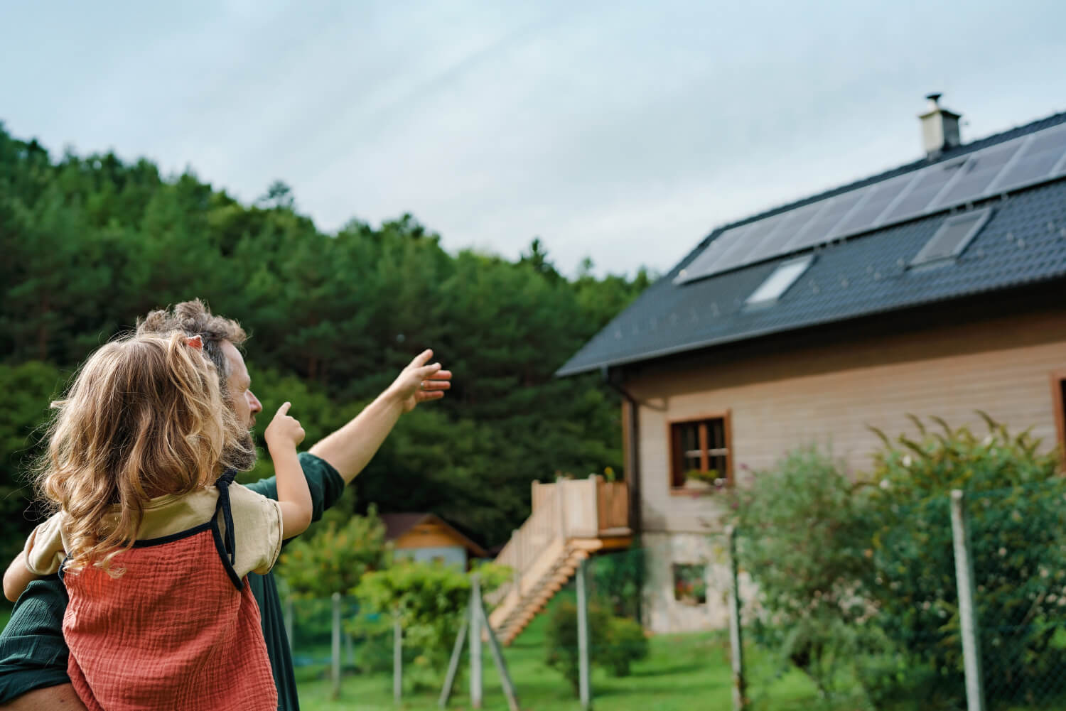 Mann mit Tochter auf dem Arm zeigen auf ein modernes Haus mit PV-Anlage