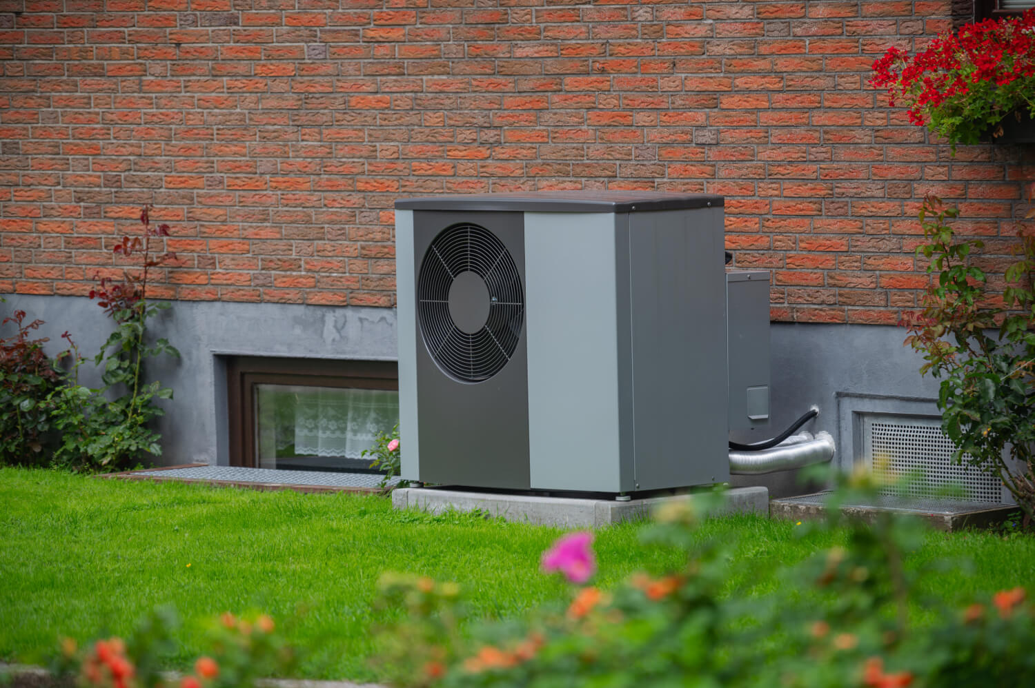 Graue Außeneinheit einer Wärmepumpe steht vor einem sanierten Altbau