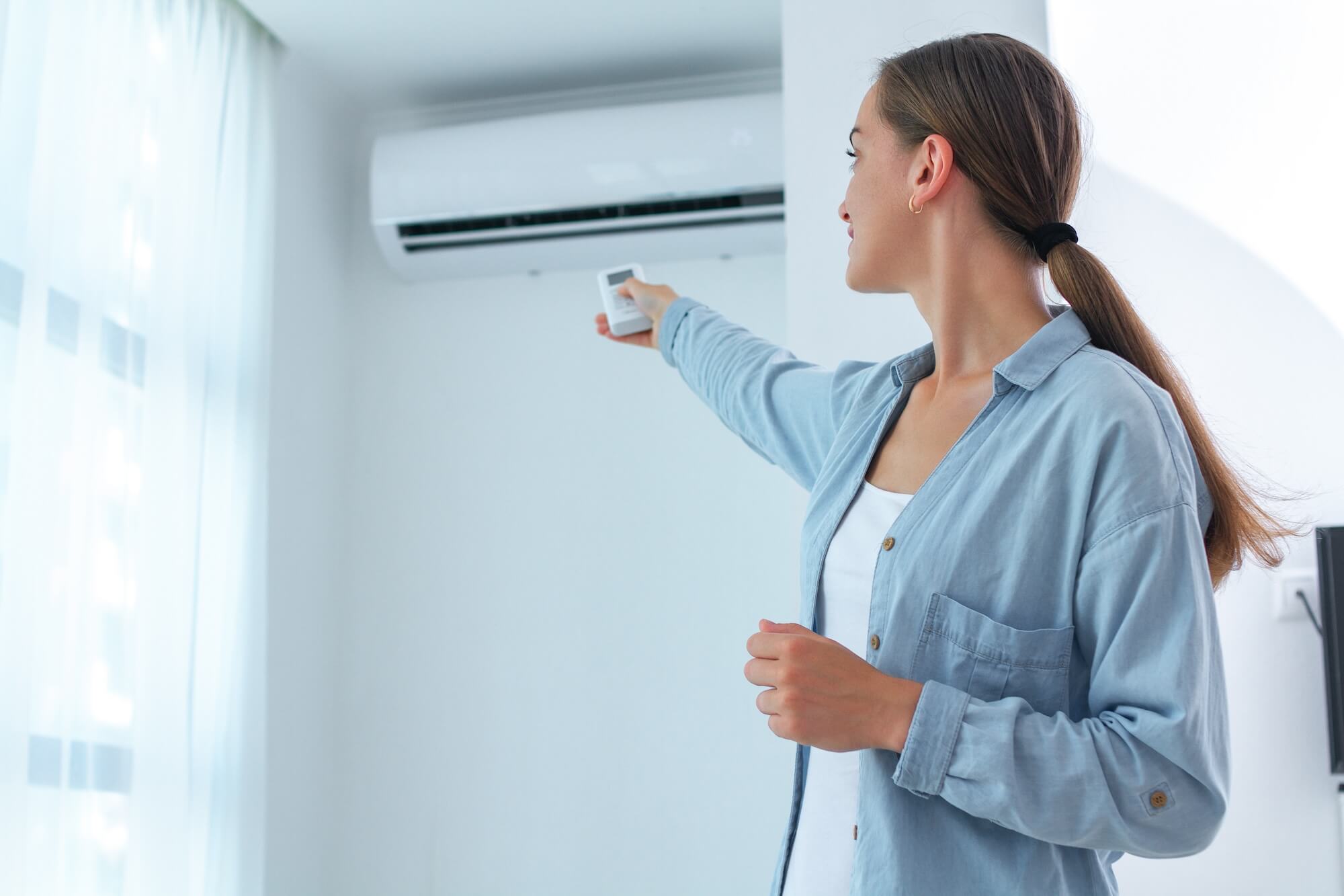 Junge Frau betätigt eine Klimaanlage im Haus