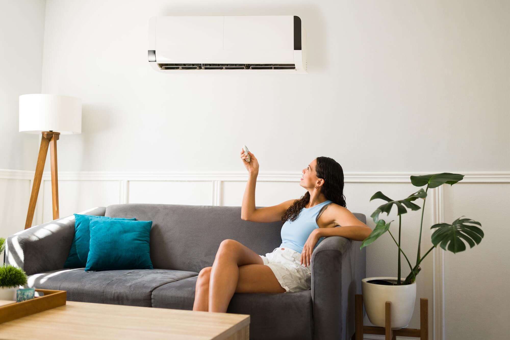 Junge Frau aktiviert eine Klimaanlage im Haus