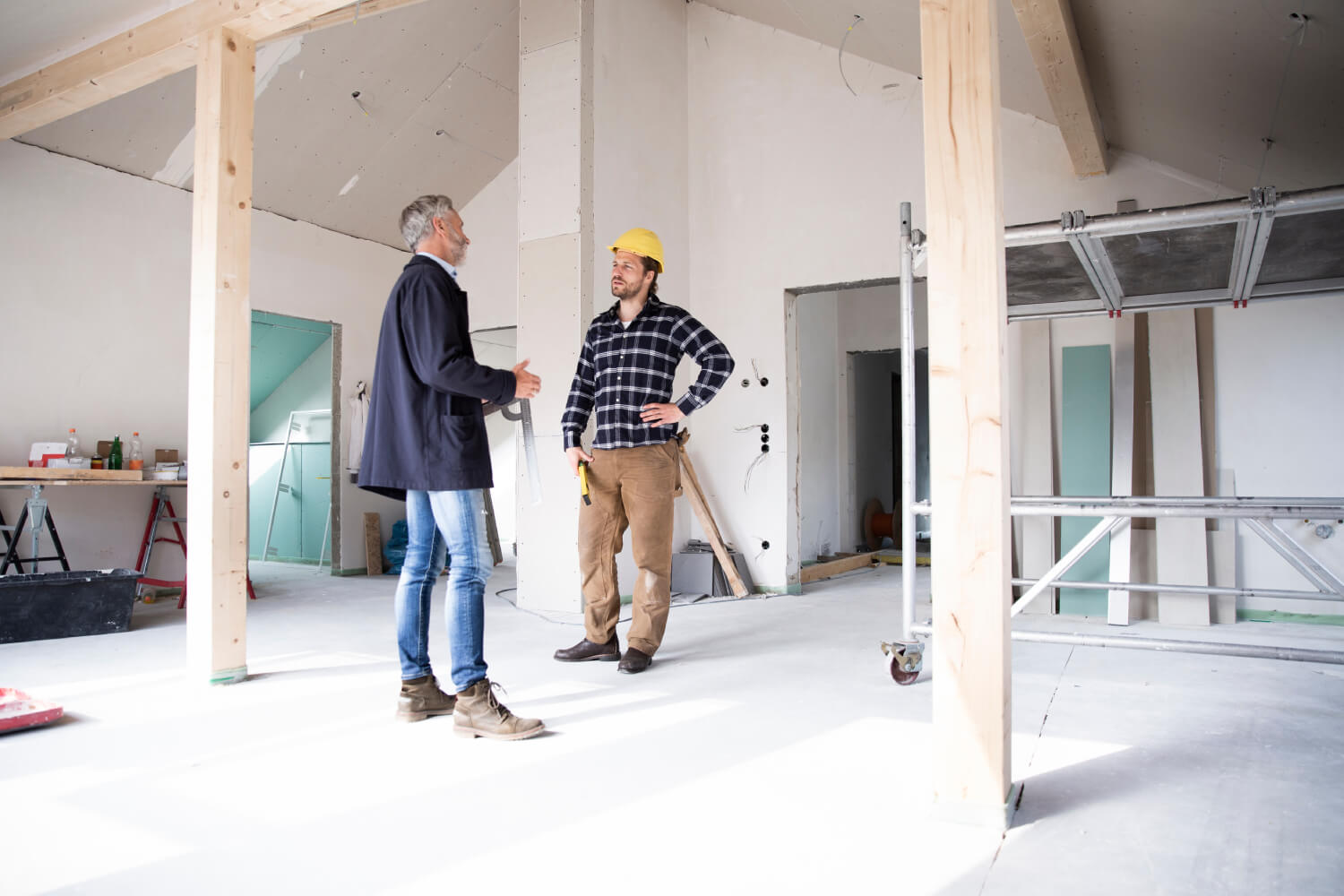 Handwerker und Hausbesitzer stehen im ausgeboten Dachboden eines Hauses und besprechen die Arbeiten