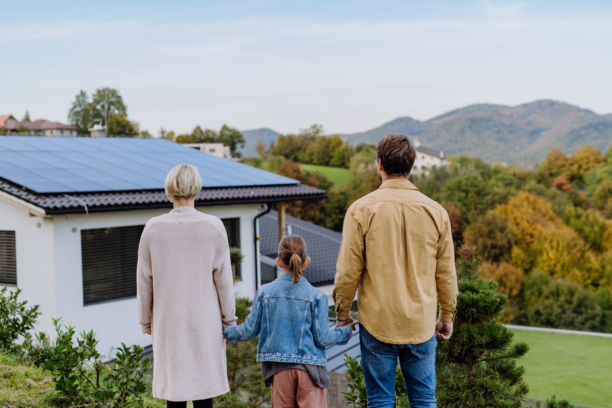 Familie steht vor Haus mit Photovoltaik auf dem Dach