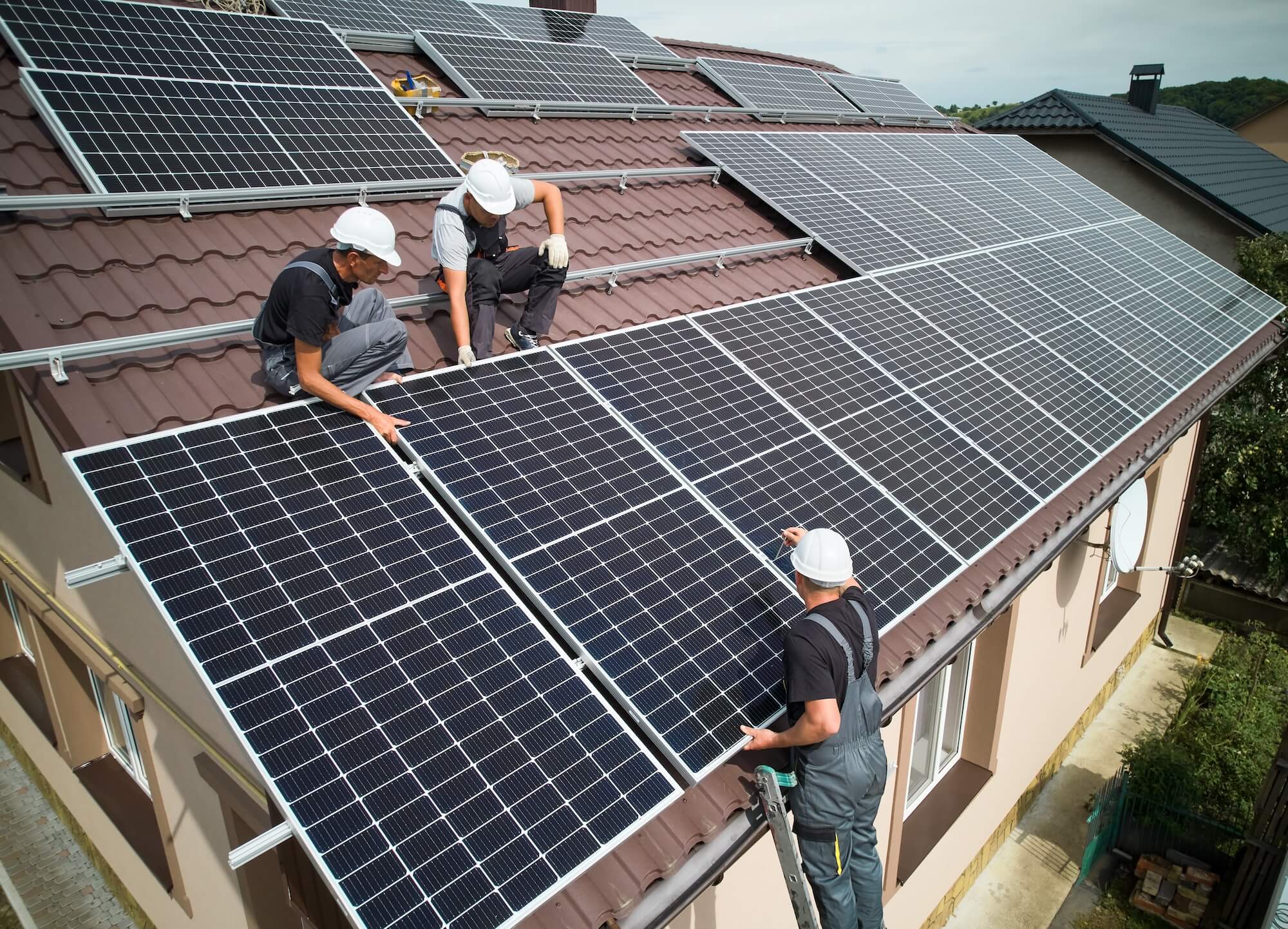 Drei Handwerker installieren eine Photovoltaikanlage auf dem Dach eines Wohnhauses.
