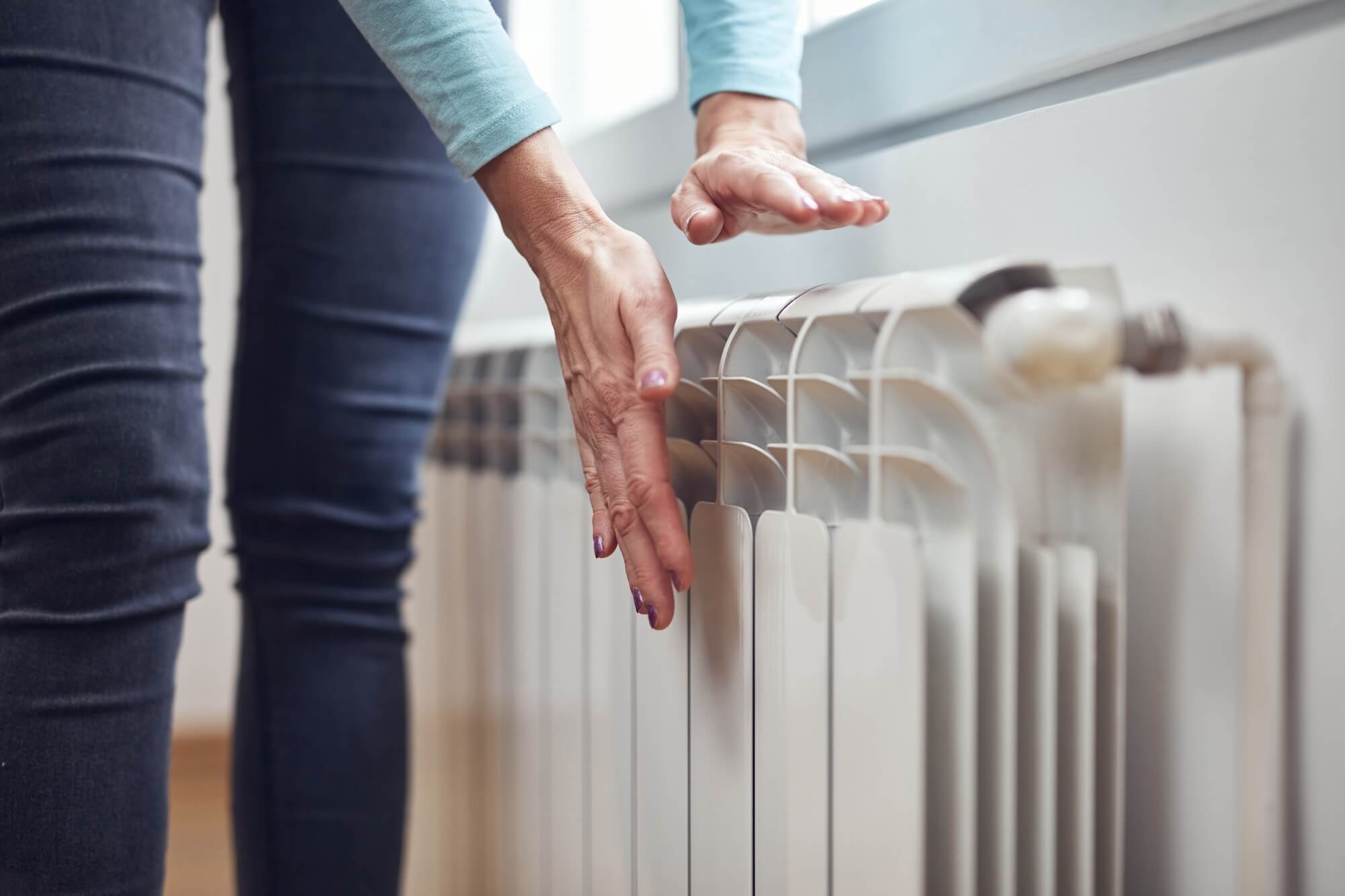 Eine Frau steht vor einem Niedertemperatur-Heizkörper und hält ihre Hand davor.