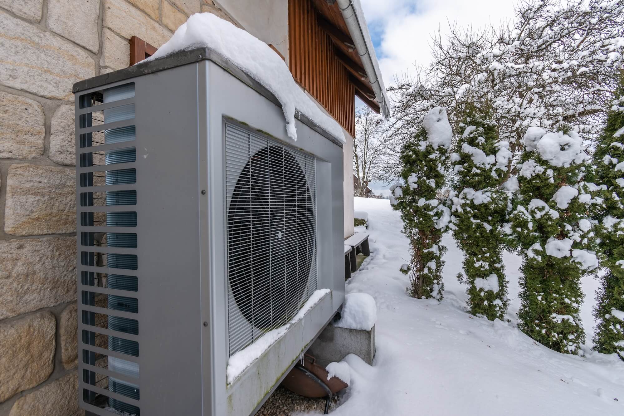 Verschneite Wärmepumpe steht vor einem Haus.