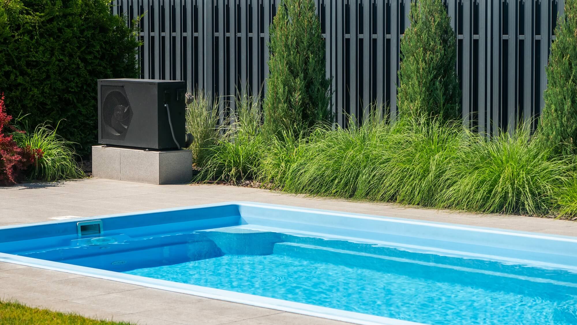 Neben einem Pool steht eine Wärmepumpe als Poolheizung