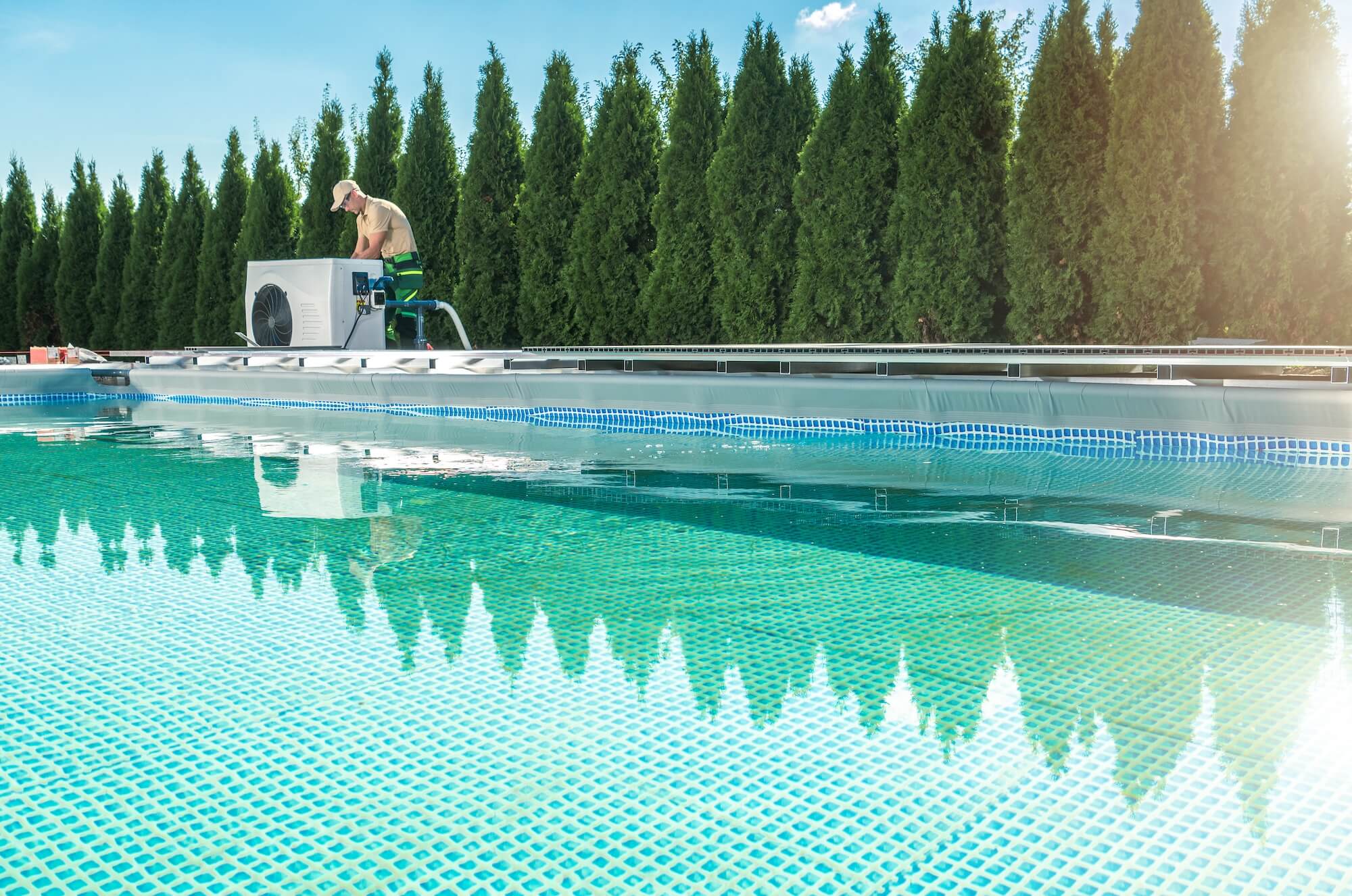 Eine kleine Pool-Wärmepumpe steht neben einem Pool.