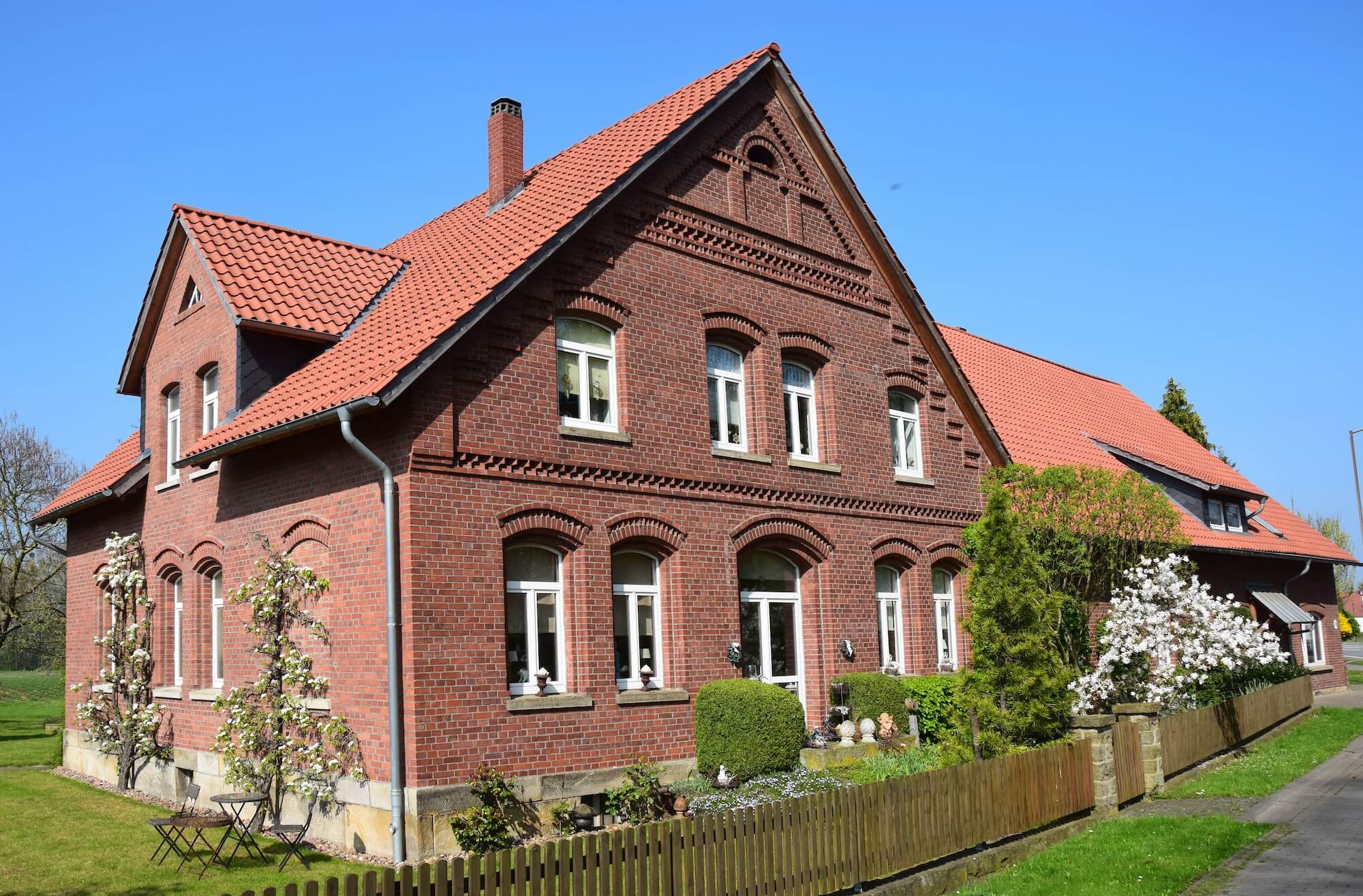 Ein altes, rotes Backsteinhaus mit weißen Fenstern steht an einer Straße.