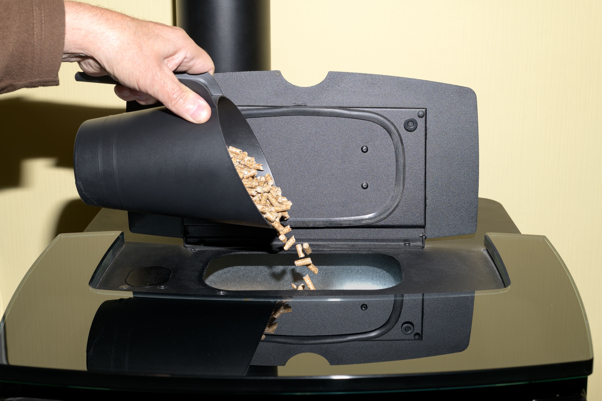 Person schĂĽttet Pellets in Pellet-Ofen-Ă–ffnung
