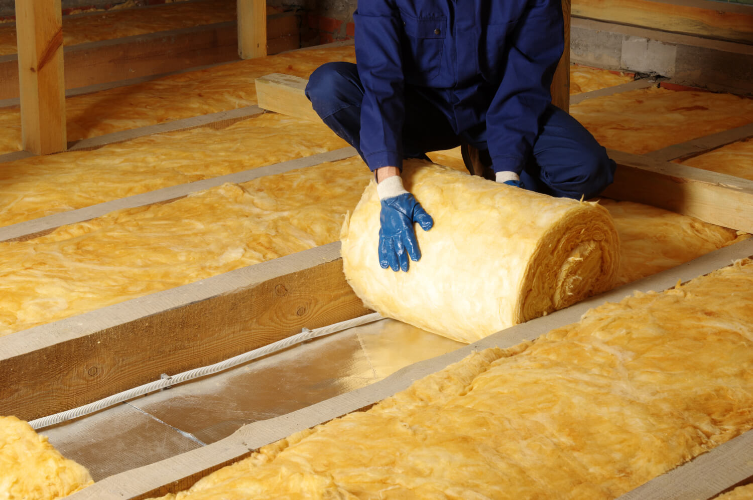 Handwerker rollt Mineralwolle im Dachboden als Dämmung aus