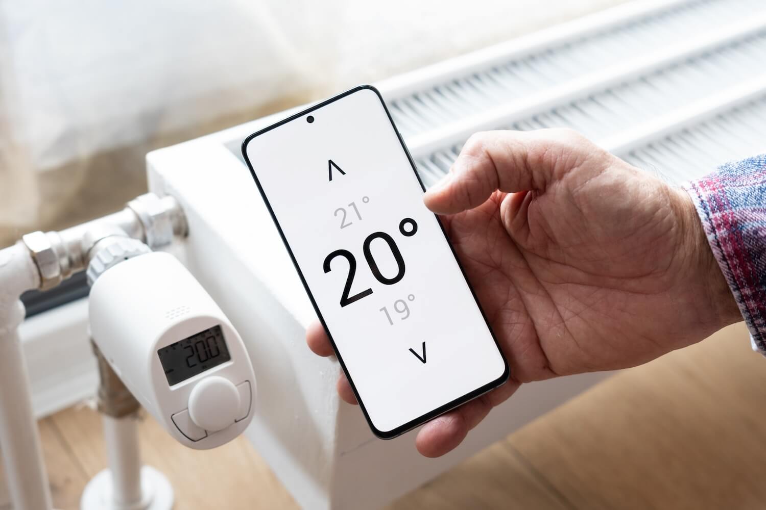 Hand hält ein Smartphone mit Temperaturanzeige zur Steuerung der Heizung per App.
