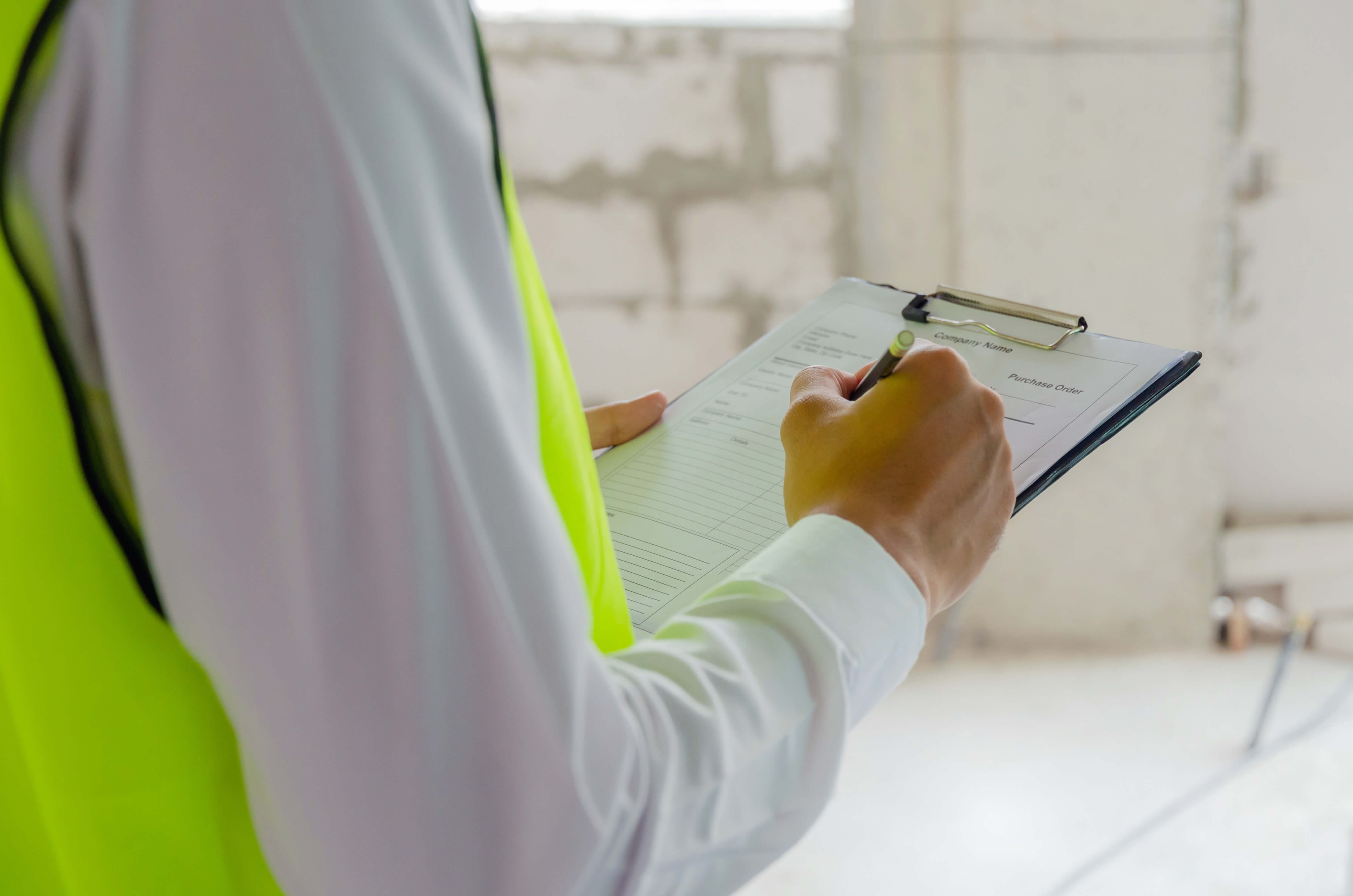 Eine Person mit gelber Warnweste steht mit Klemmbrett auf einer Baustelle.