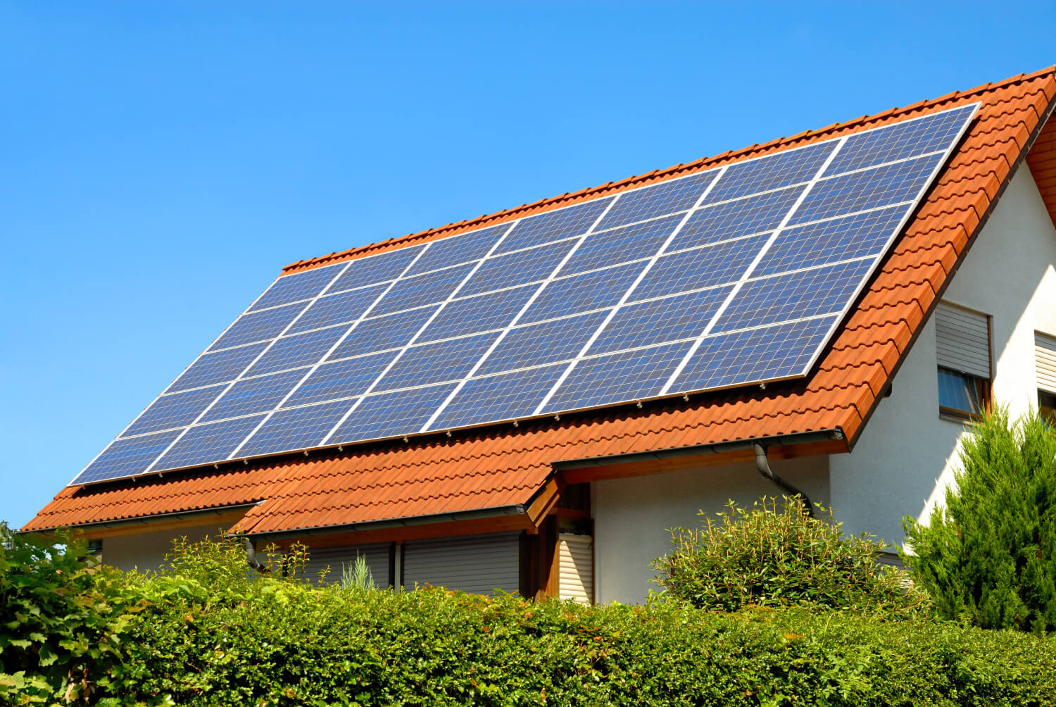 PV-Anlage mit Smart Meter auf dem Dach eines Hauses mit Hecken im Vordergrund
