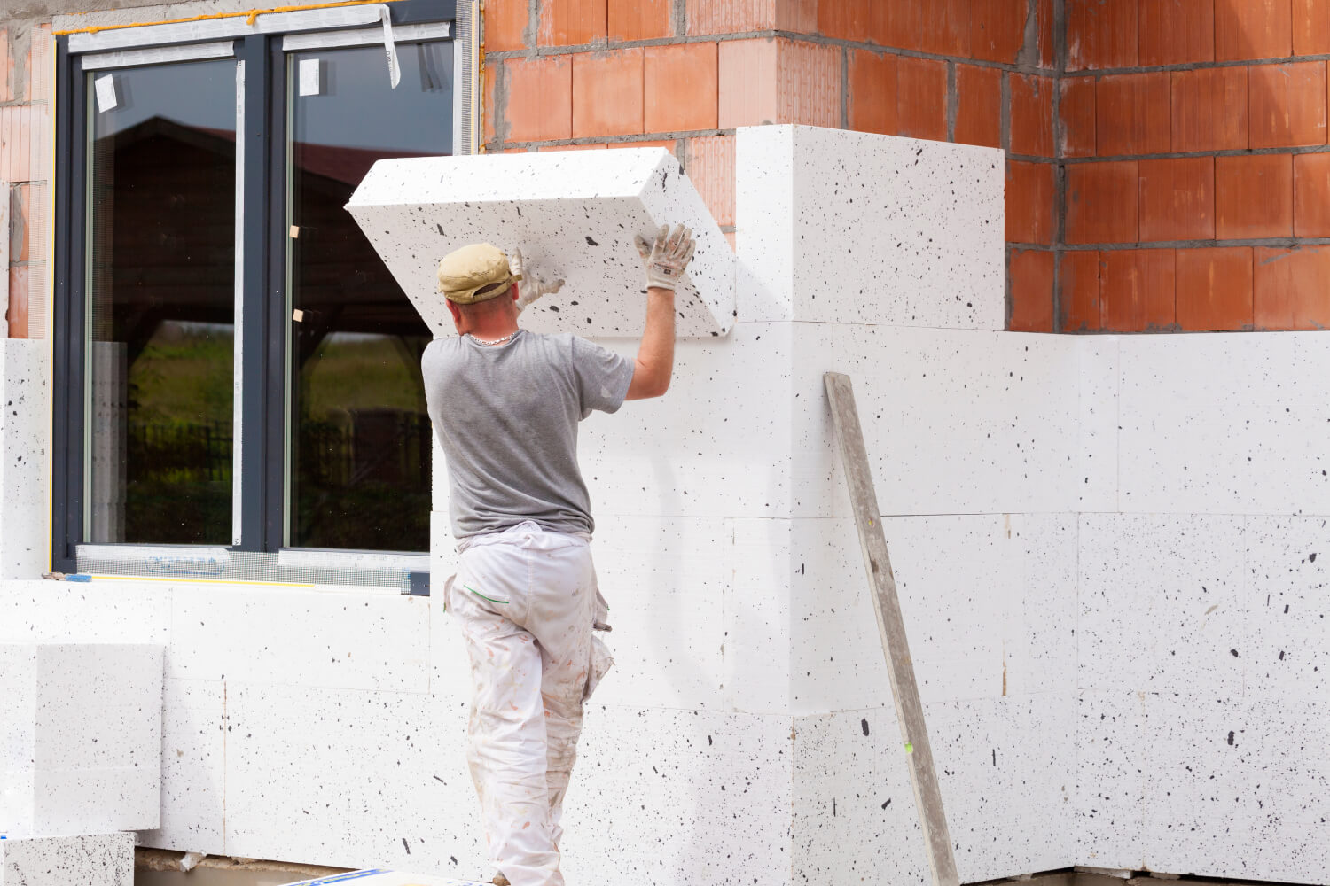 Handwerker bringt Dämmmaterial von außen an der Fassade an um ein Haus zu dämmen
