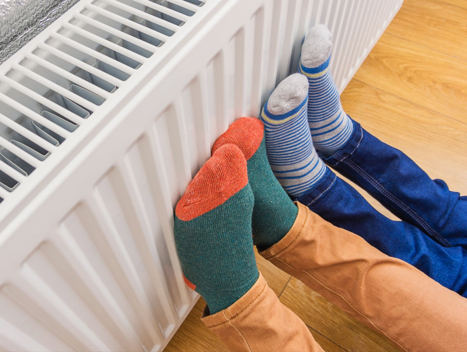 Zwei Personen wärmen Füße am Radiator nach hydraulischem Abgleich Pflicht-Durchführung