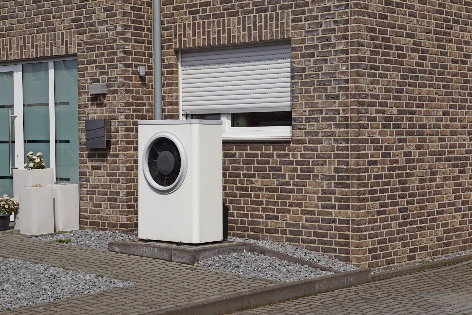 Weiße Luft-Wärmepumpe vs. Erdwärmepumpe Vergleich - Außeneinheit vor modernem Klinkerhaus installiert