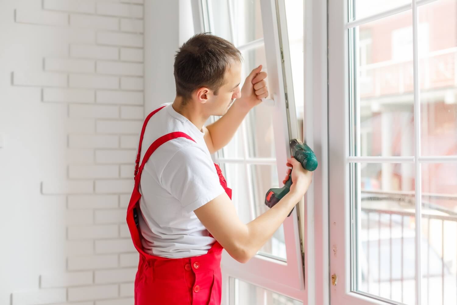 Handwerker fĂŒr Fenster bei der Installation eines neuen Fensters mit elektrischem Schraubendreher