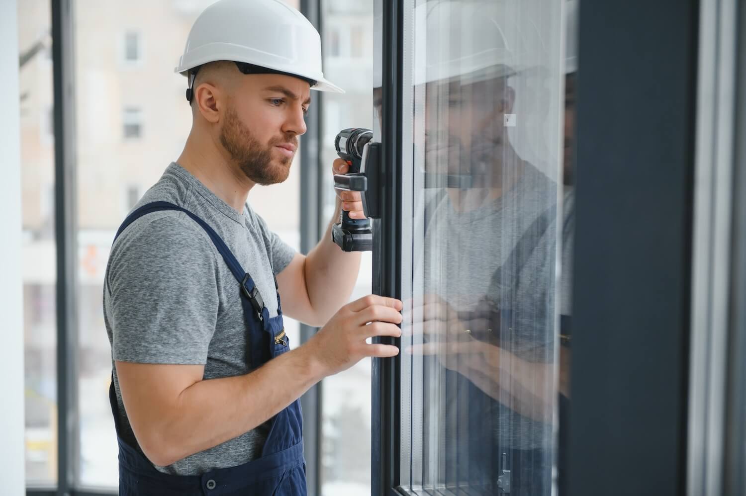 Professioneller Handwerker fĂŒr Fenster fĂŒhrt Montagearbeiten mit Bohrmaschine am Fensterrahmen durch