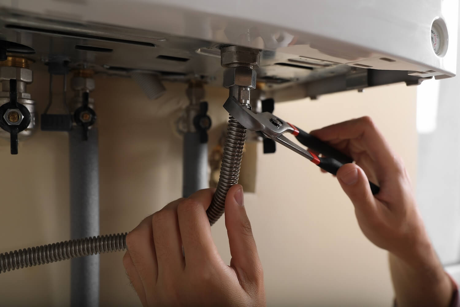 Nahaufnahme eines Handwerkers beim Anschluss eines flexiblen Edelstahlrohrs an eine neue Gasheizung.