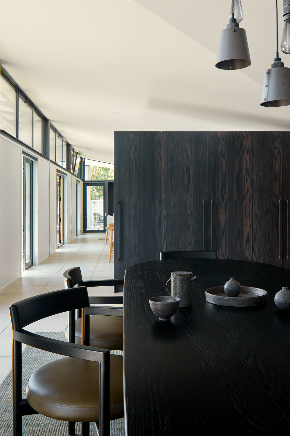 Black round dining table and leather chairs beside dark timber cabinetry