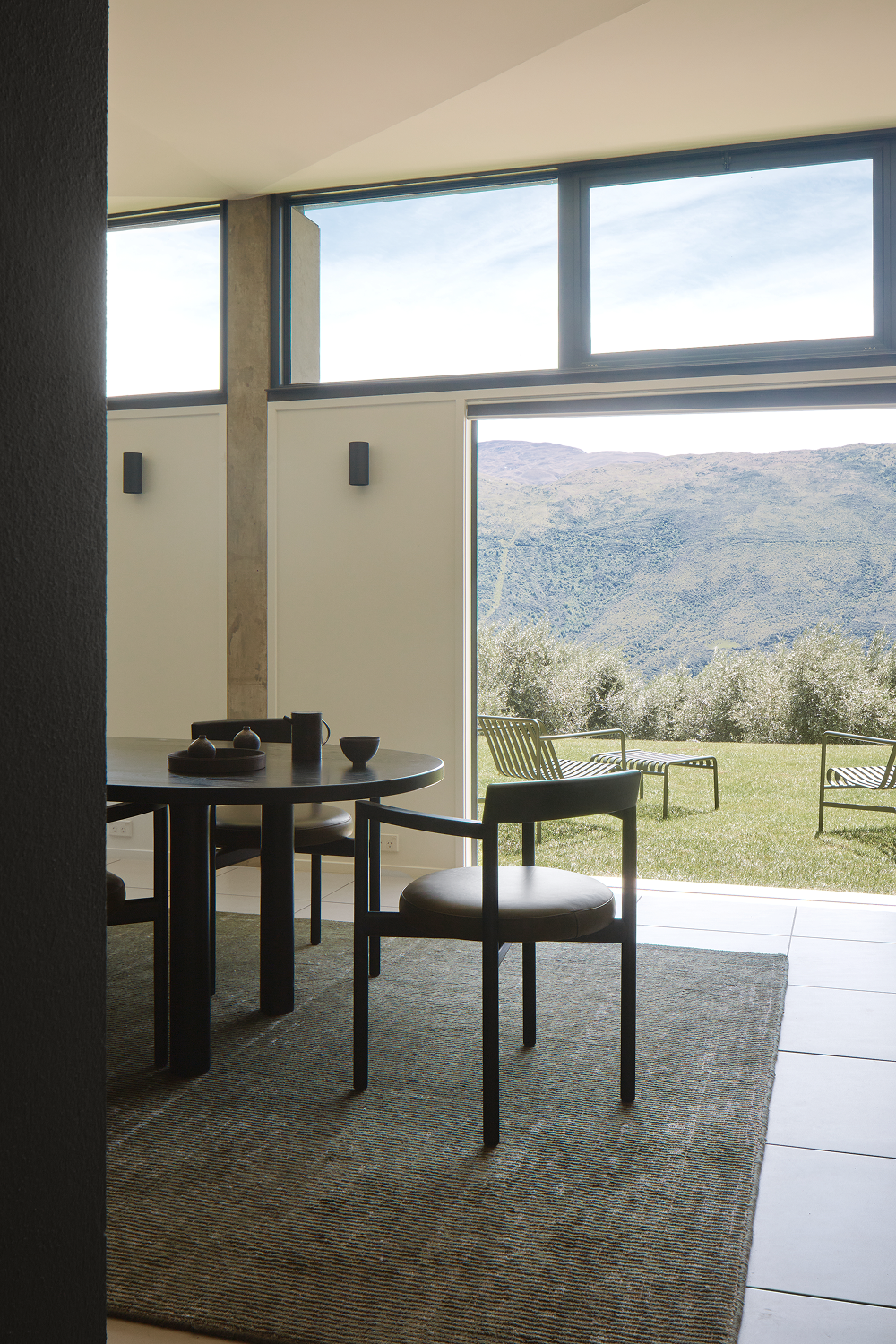 Black dining table and chairs on rug facing mountain view through window