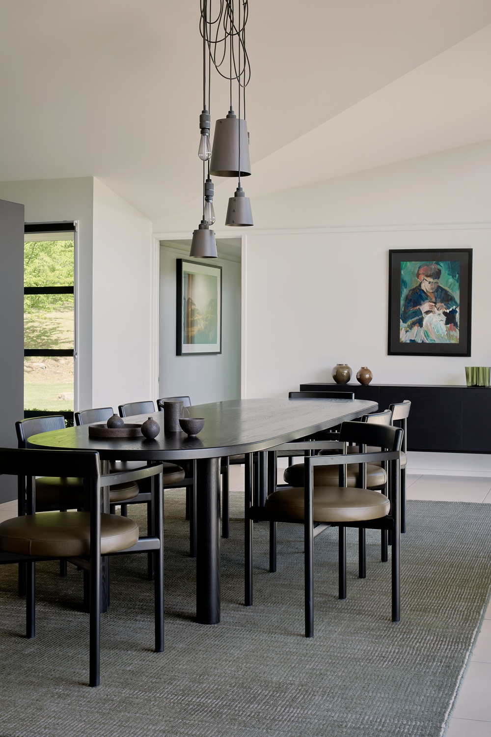 Black oval dining table with leather chairs and hanging pendant lights
