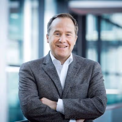 Man in suit smiles with arms crossed.