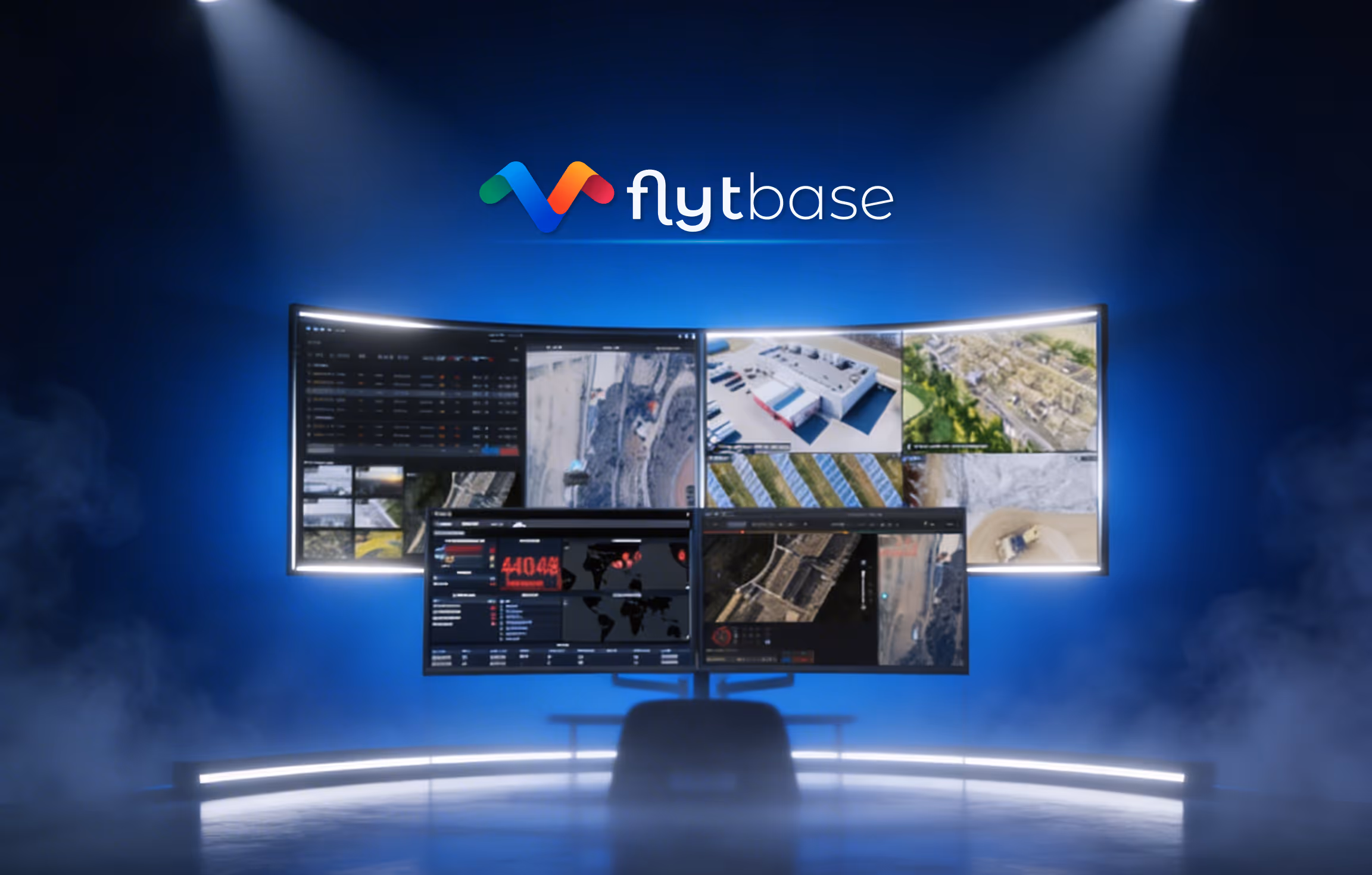 Four curved monitors on a stand displaying various aerial and map views with the Flytbase logo above them against a blue background.