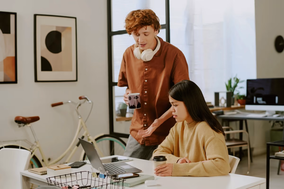 Young man and woman discussing something on a laptop in a modern office, with a bicycle in the background.