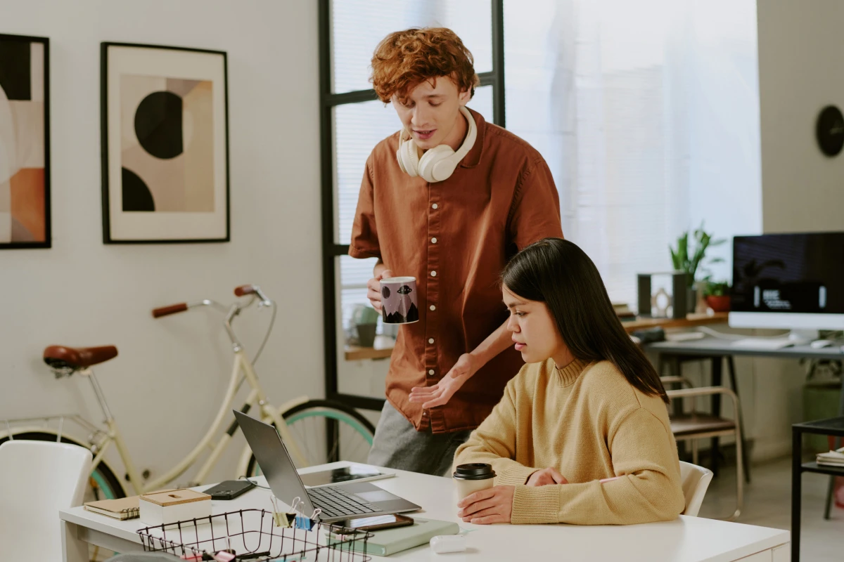 Young man and woman discussing something on a laptop in a modern office, with a bicycle in the background.